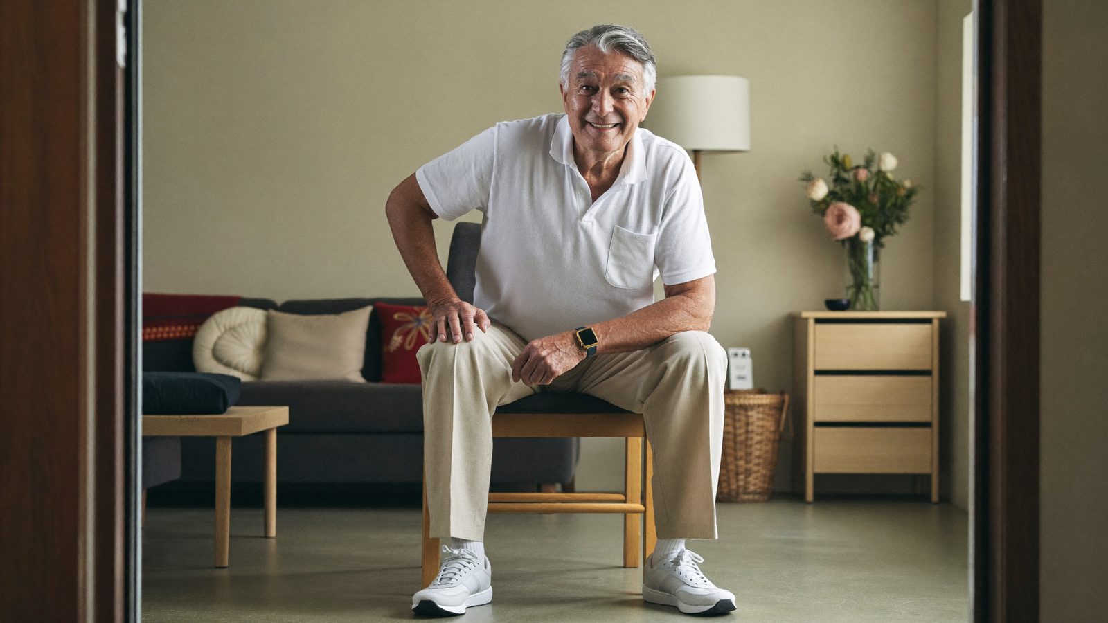 Senior man practicing a gentle balance exercise while holding the back of a sturdy chair at home