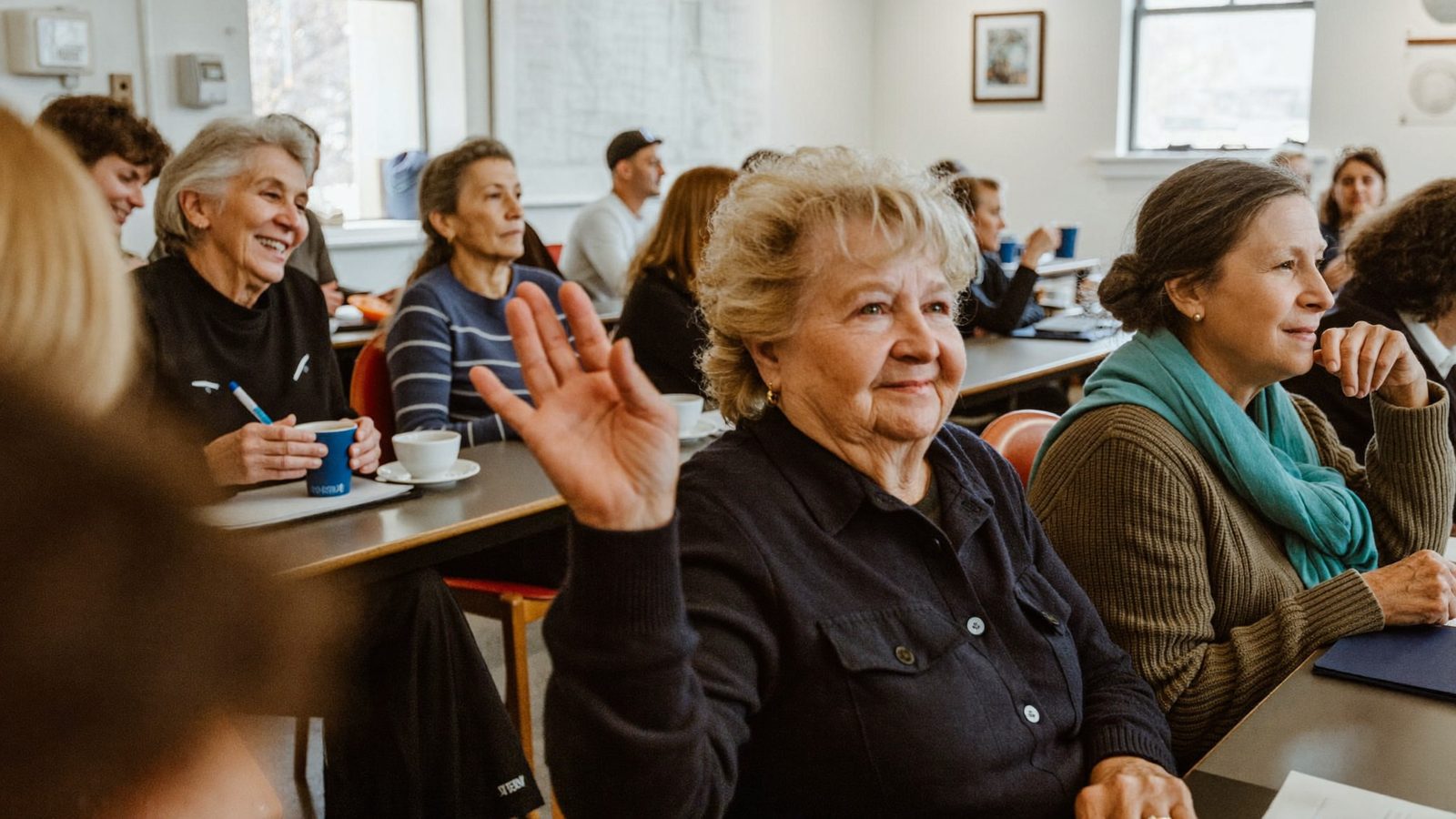 Seniors seated in a bright community room raising hands to ask questions at a Medicare educational presentation