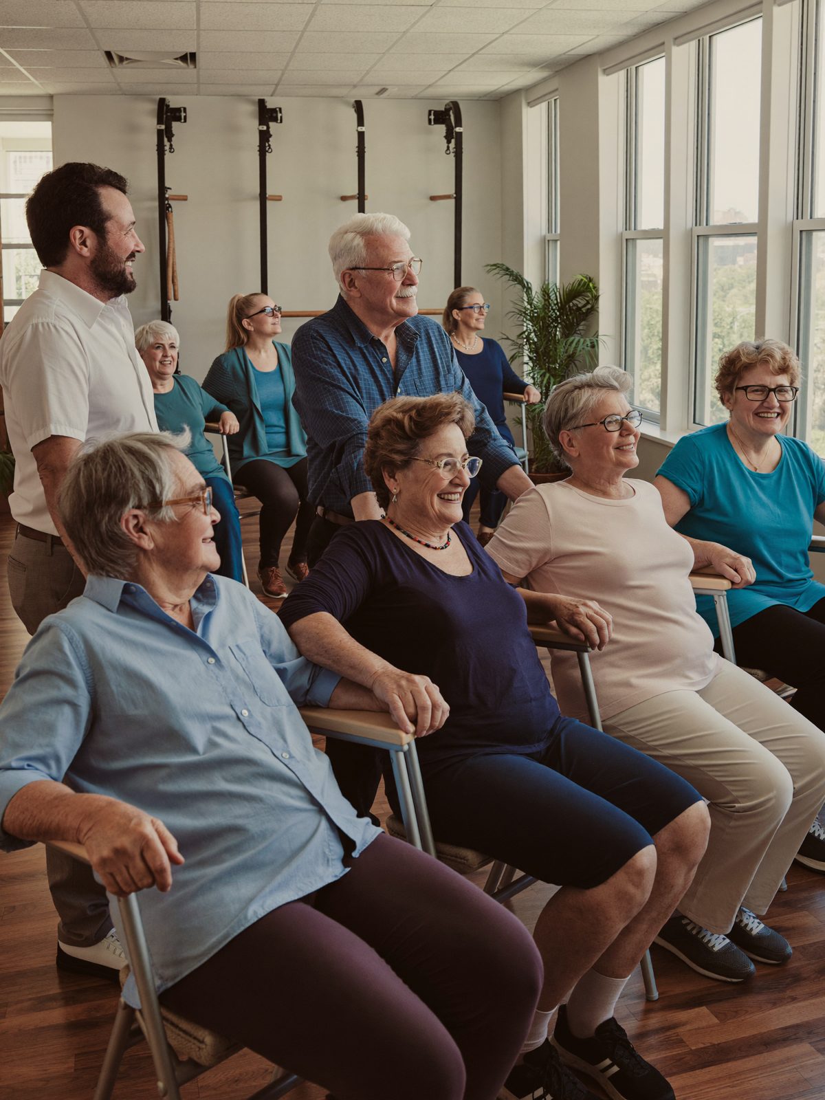 Personas mayores practicando ejercicios suaves de equilibrio con sillas en un salon comunitario luminoso en Oak Creek Senior Villas
